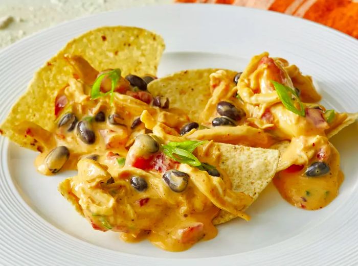 A high-angle view of a plate of tortilla chips, topped with chicken nacho dip, black beans, and green onions.