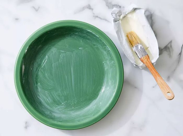 An earthy green round pie dish, coated with shortening.