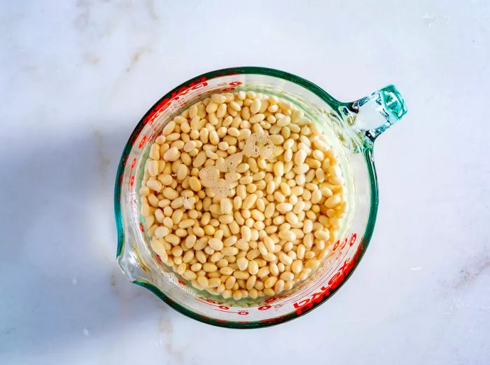 A top-down view of a measuring cup filled with beans soaking in water