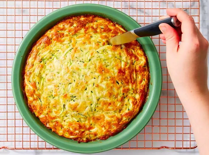 The zucchini pie, perfectly baked to a golden brown, with a knife inserted in the center coming out clean.