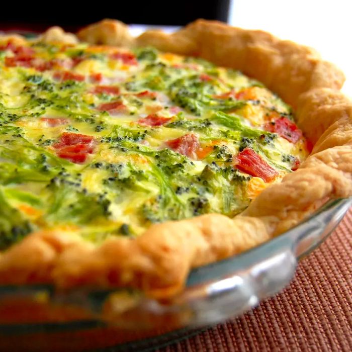 A close-up shot of a delicious quiche filled with broccoli and bacon, served in a glass pie dish.