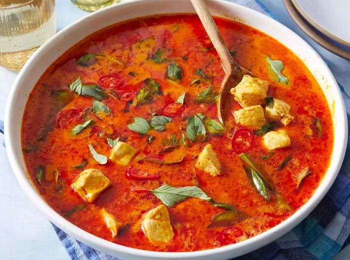 High-angle shot of a bowl filled with Panang curry, chicken, and vibrant fresh herbs