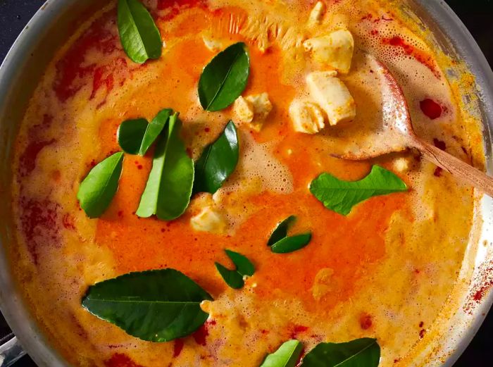 Aerial view of Panang curry with chicken being cooked, with lime leaves being added