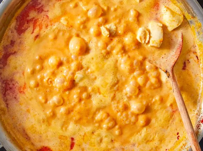 Aerial view of Panang curry with chicken simmering in a pan, stirred with a wooden spoon