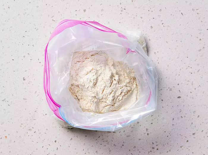 A zip-top bag containing flour, garlic powder, salt, and pepper.