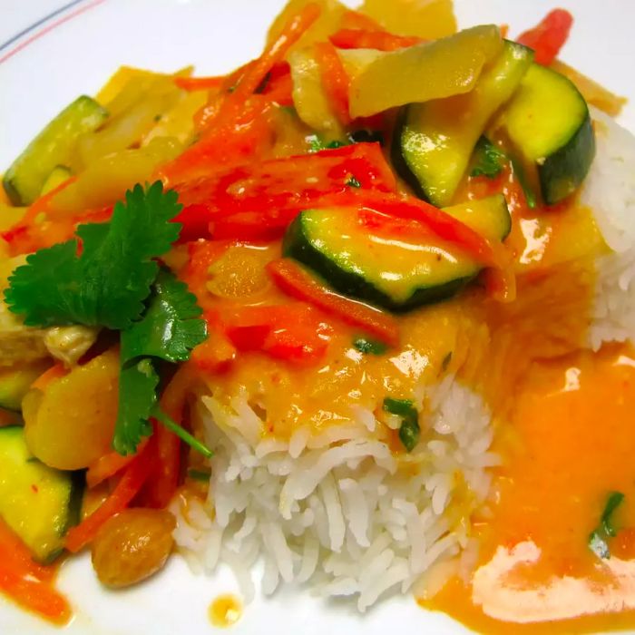 Close-up of Thai Red Chicken Curry, garnished with fresh herbs, served over white rice on a white plate