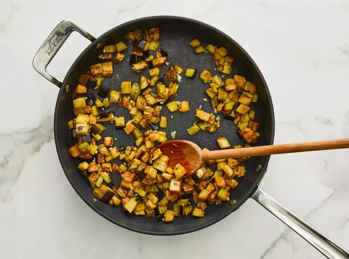 Top-down view of diced eggplant being sautéed in a skillet