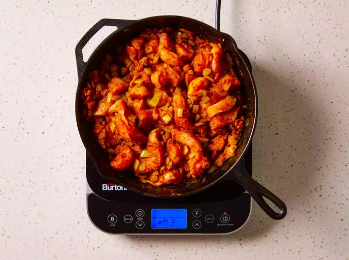 Onions, chicken, and curry powder simmering together in a cast iron skillet on a burner