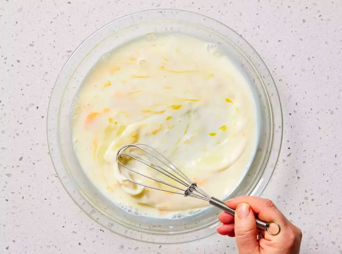 A shallow bowl with egg and milk being whisked together.