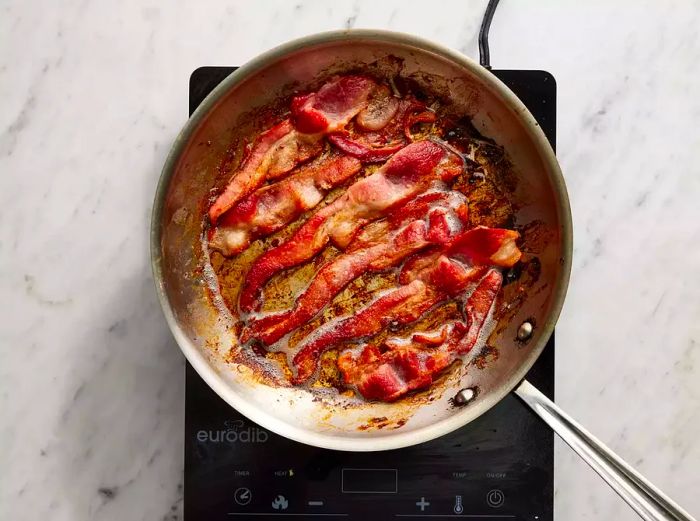 Bacon frying in a skillet until golden and crispy.