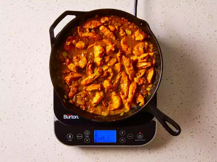 Easy Chicken Curry simmering in a cast iron pan on the stovetop