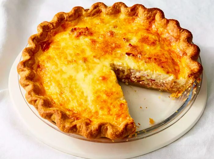 An overhead view of a pie dish with a slice of Quiche Lorraine missing.