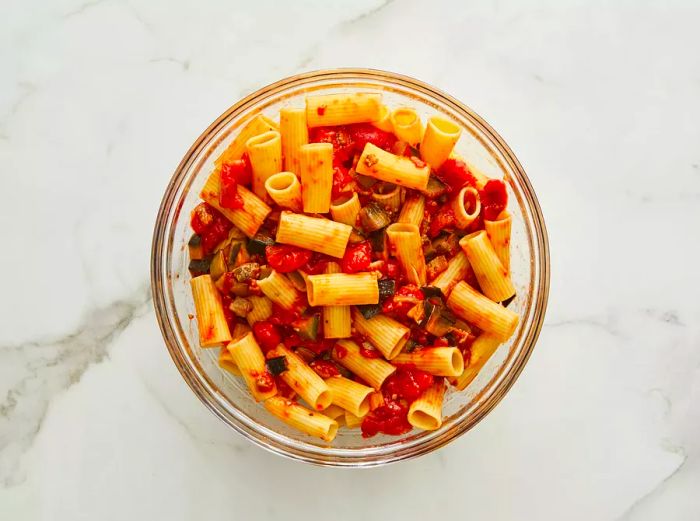 A bowl of pasta topped with a rich eggplant and tomato sauce, shot from above