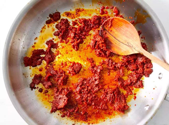 Aerial view of curry paste simmering in a pan, being stirred with a wooden spoon