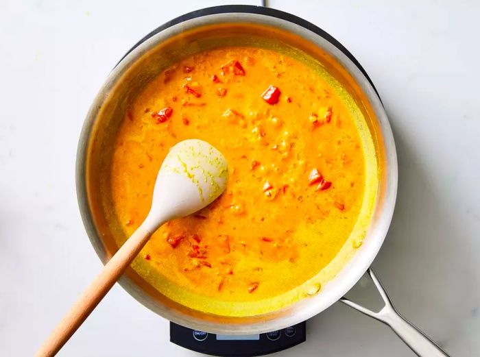 A pan of curry sauce being stirred with a wooden spoon