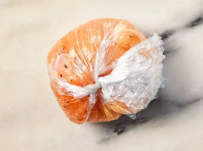 A plastic-wrapped chicken ball, filled with herb butter