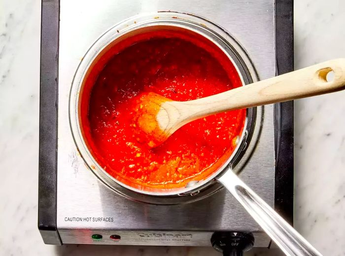 The pizza sauce is gently simmering in a small saucepan.