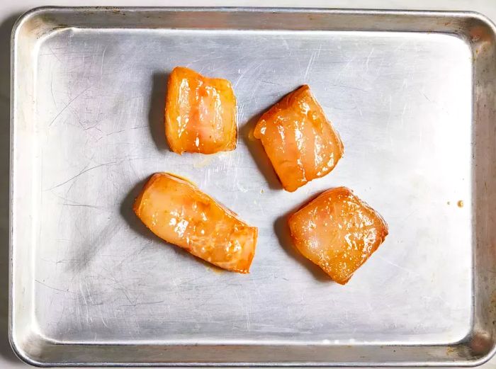 A top-down view of marinated Chilean sea bass fillets arranged on a baking sheet.