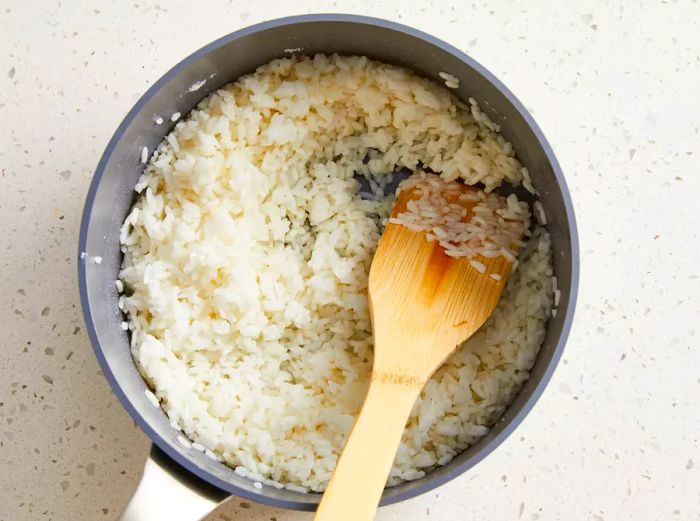 An overhead view of rice simmering in a pot, stirred with a wooden spatula