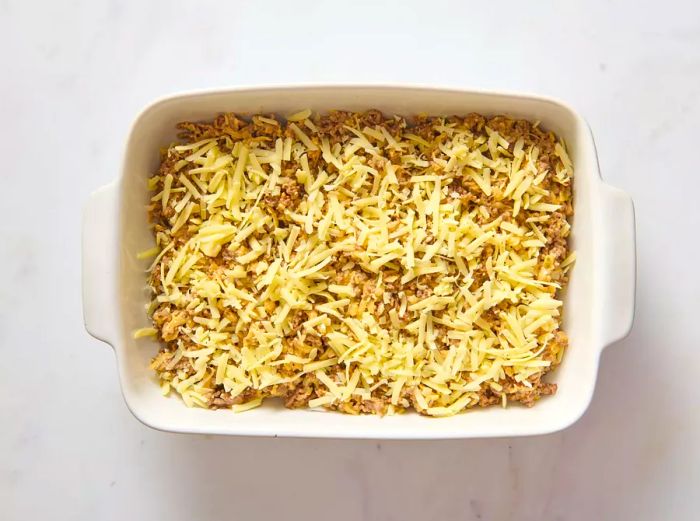 A baking dish layered with hash brown patties, topped with the ground beef mixture and melted shredded cheese