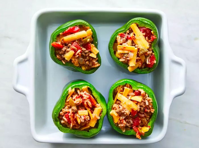 A top-down view of stuffed green peppers with melted cheese, placed in a baking dish