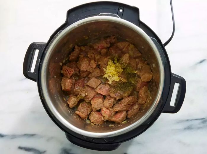 An Instant Pot with browned beef chunks topped with garlic and thyme