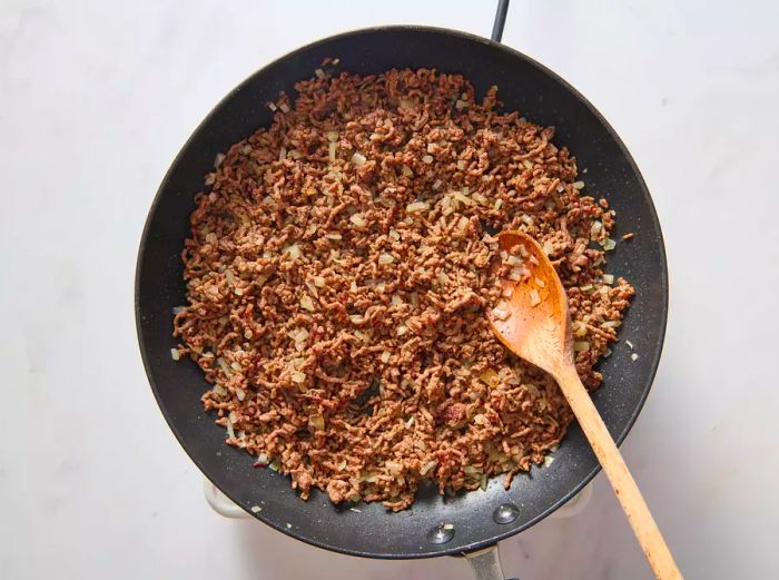 A large skillet with browned ground beef and chopped onions