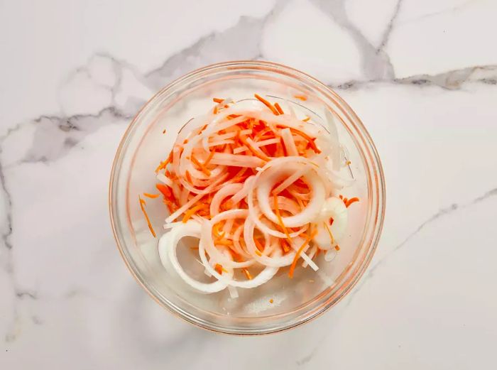 A small bowl filled with sliced onions and carrots immersed in pickling liquid