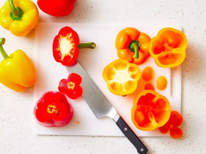 A cutting board with bell peppers, their tops removed and bottoms trimmed for stability.