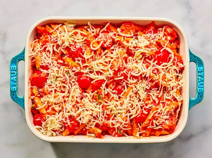 A baking dish filled with creamy tomato penne pasta, topped with a generous layer of shredded mozzarella cheese.