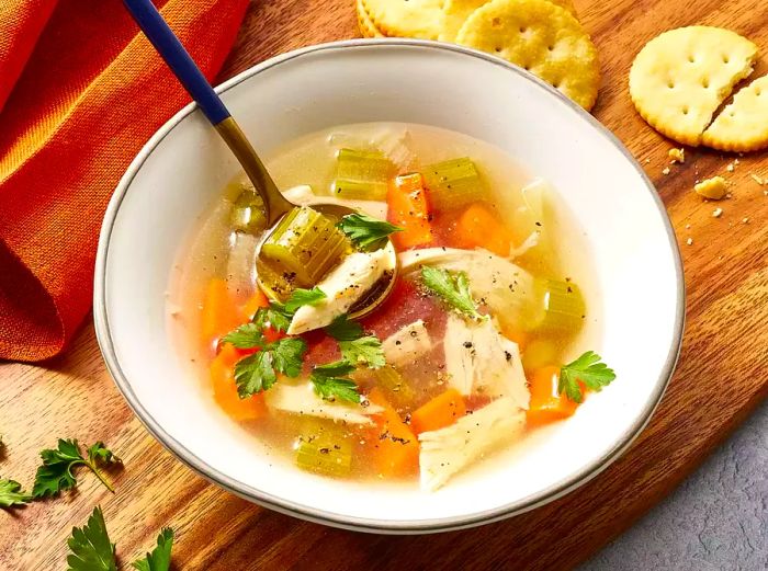 Homemade chicken soup garnished with fresh parsley and served alongside crackers.