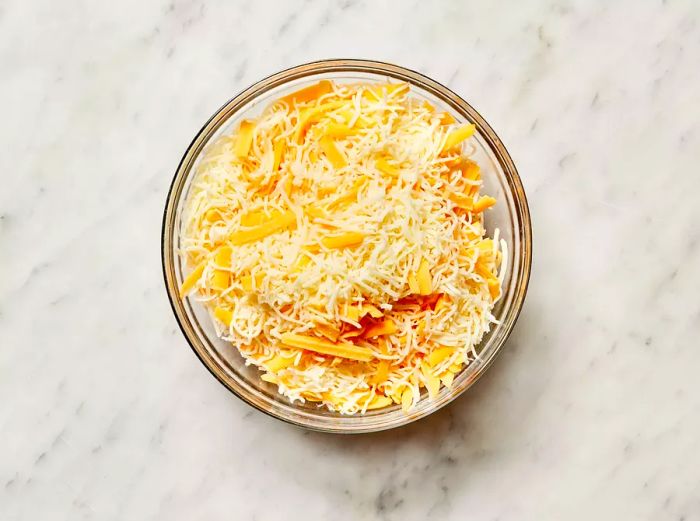 A top-down view of a mixture of Cheddar and Monterey Jack cheese in a glass mixing bowl.