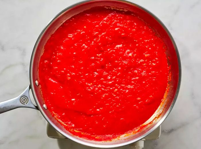 A pan with tomato sauce and tomato paste, along with chopped onions and garlic.