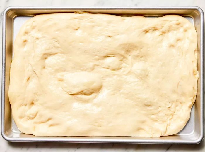 The pizza dough has doubled in size after resting on the rectangular baking sheet.