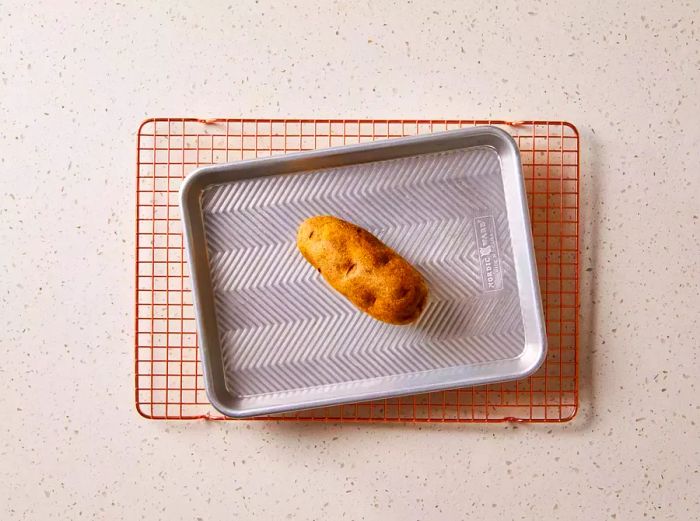 Potato resting on a baking sheet atop a cooling rack