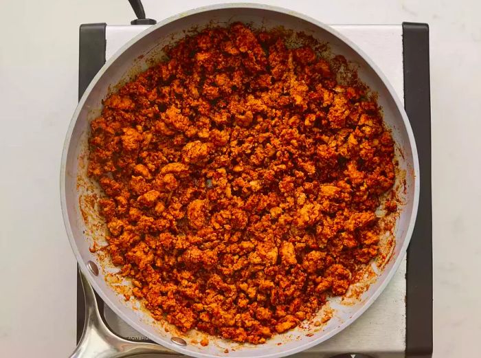 A large skillet with seasoned ground turkey and water mixture