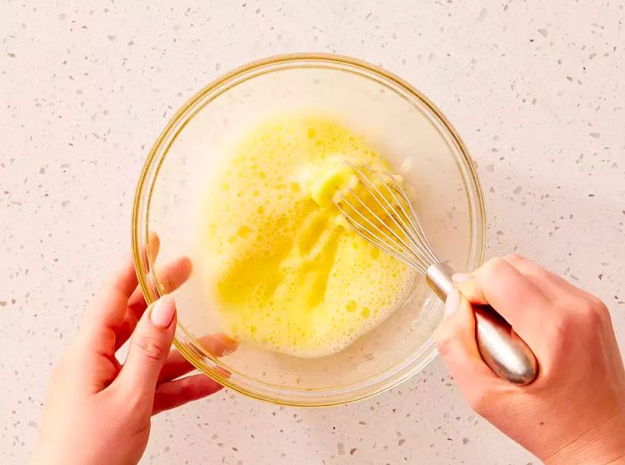 A bowl of beaten eggs and water, being mixed together into a frothy blend