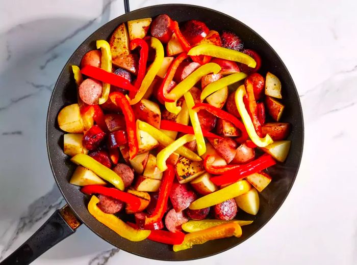 Kielbasa, potatoes, and peppers sautéing together in a skillet.