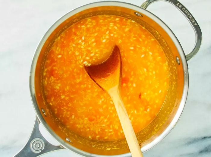 An overhead view showing white wine, chicken stock, and mashed butternut squash being added to a saucepan, with a wooden spoon in the mix.