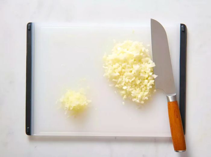 A cutting board with a pile of grated onion and a separate pile of diced onion