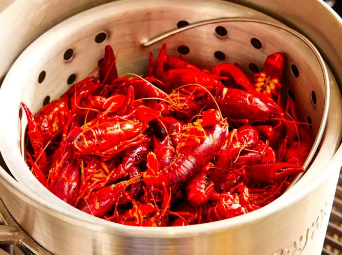 A large pot with a steamer basket, topped with whole crawfish over the sausage and vegetables.