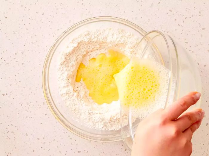 A large bowl containing flour and salt, with egg being poured into the center of the mixture