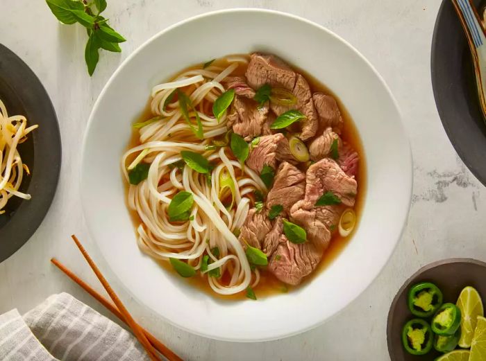 An overhead view of pho in a white bowl, with chopsticks placed on the side.