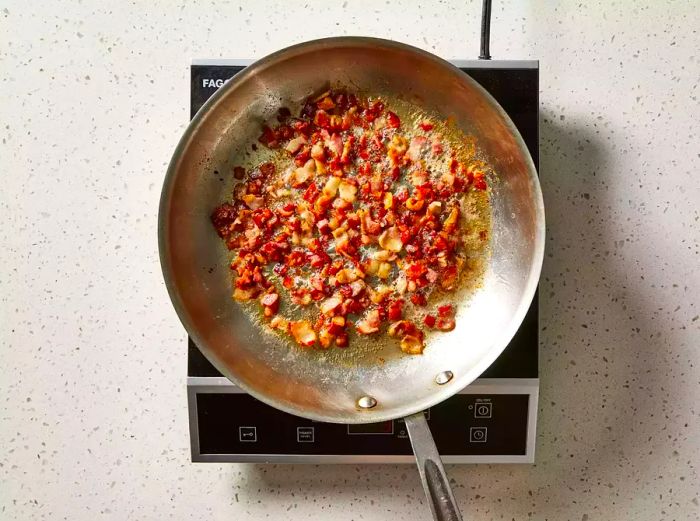 Bacon cooked in a skillet until it reaches a crispy, golden-brown texture.