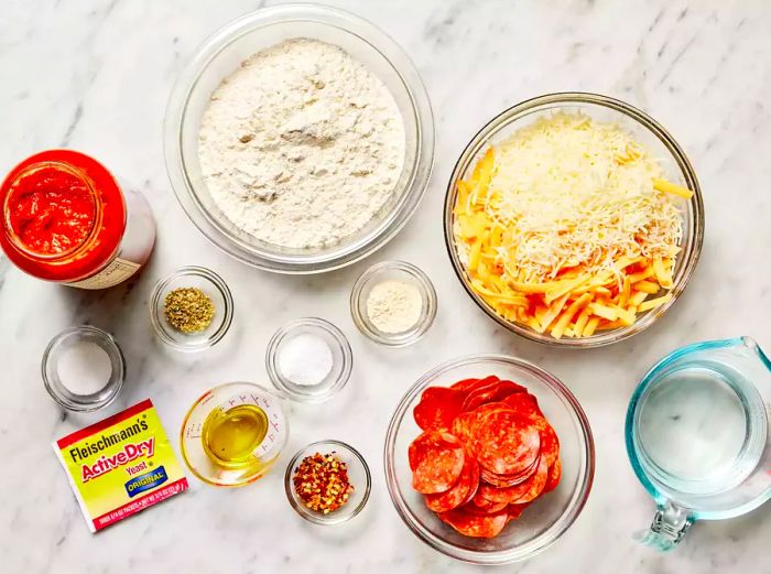 A bird's-eye view of all the ingredients for making a Detroit-style pizza arranged neatly on a marble countertop.