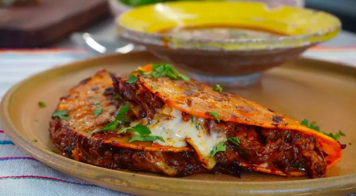 A close-up of Birria de Res Tacos (Beef Birria Tacos) served with a dipping sauce and garnished with fresh cilantro.