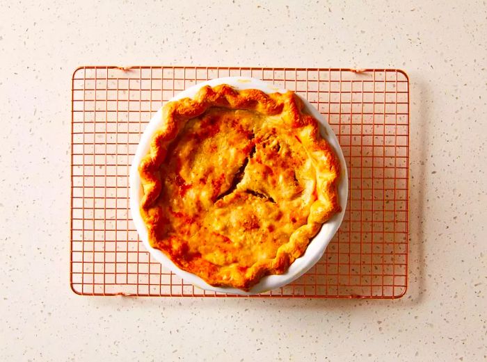 Baked Tourtière (French Canadian Meat Pie) resting on a cooling rack in its pie dish