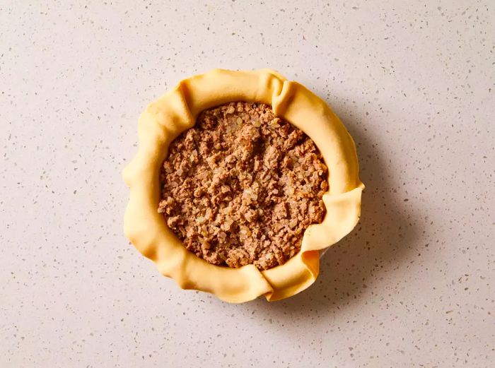 Meat filling in a pie dish with pie dough surrounding it