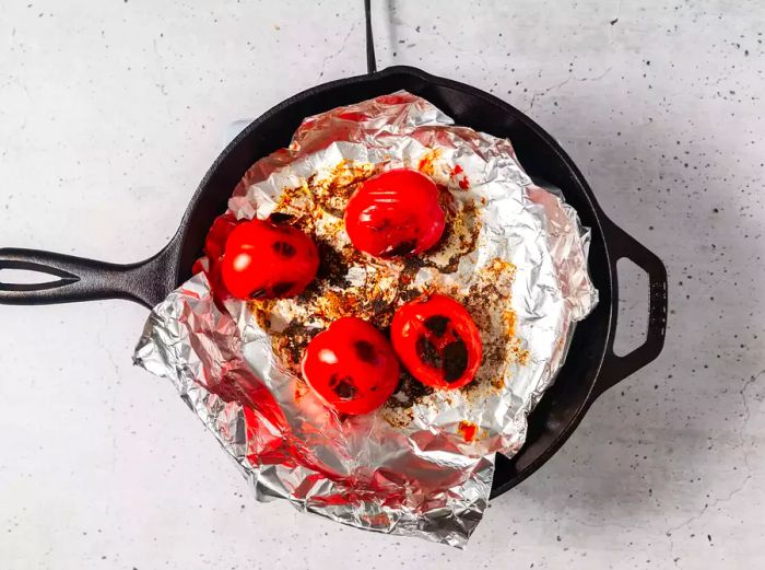 A cast-iron pan lined with aluminum foil, with blackened tomatoes on top