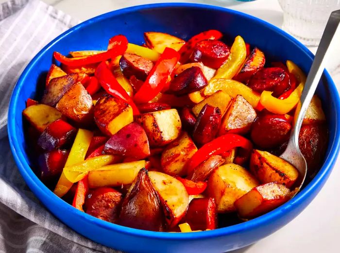 Kielbasa with peppers and potatoes, beautifully served in a blue bowl.